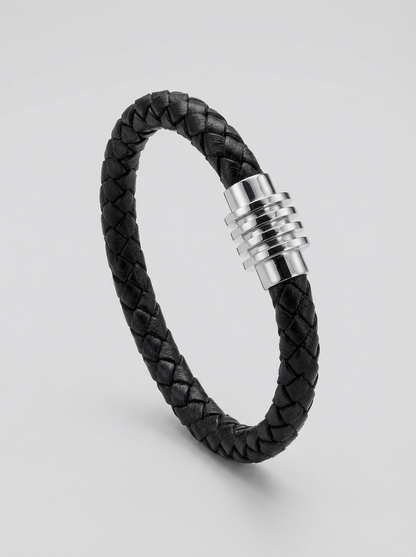 A black braided leather bracelet with a polished silver-toned metal clasp, displayed on a light gray background.