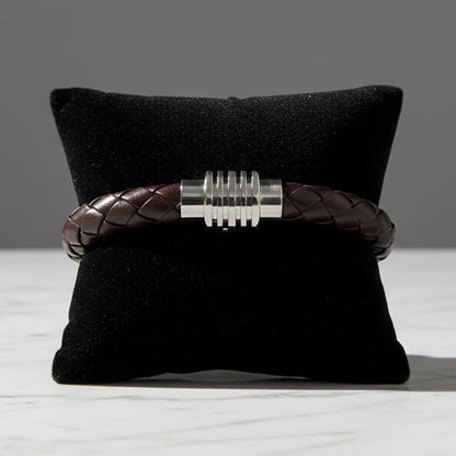 Brown leather bracelet with silver clasp on a black cushion against a white background