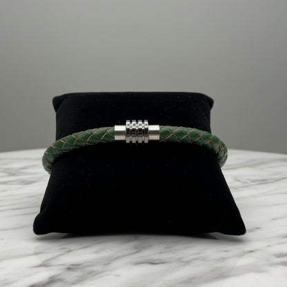 Green braided bracelet with silver circular orbit clasp on a black pillow against a light gray background