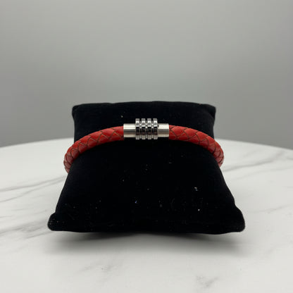 Red braided bracelet with silver Circular Orbit clasp on a black cushion against a gray background