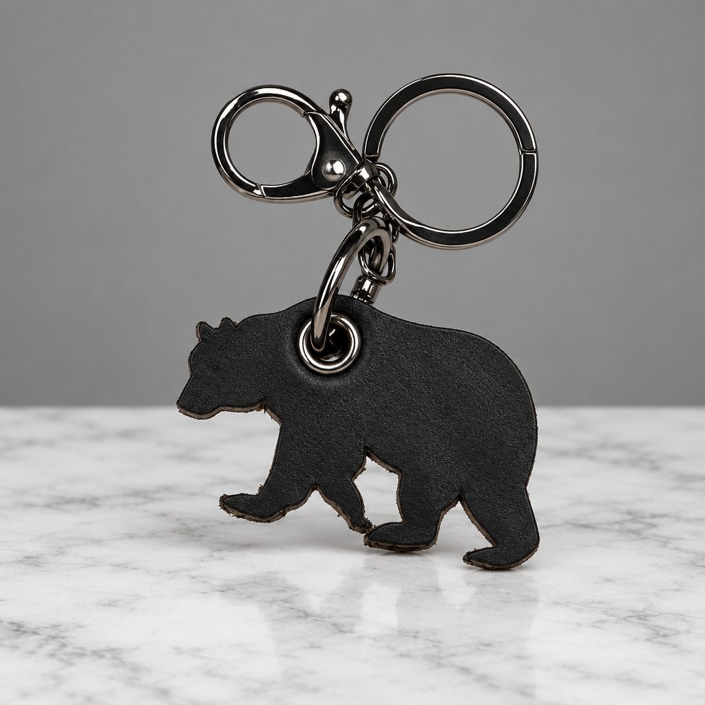 A black bear-shaped keychain charm with a silver-tone split ring and lobster clasp, shown on a light off-white textured background.