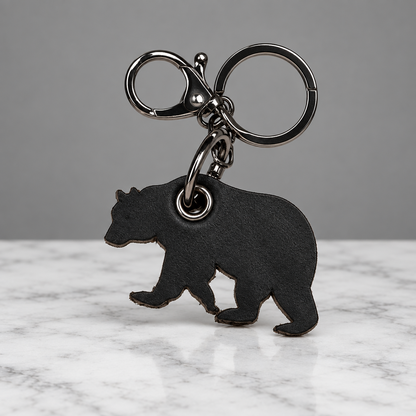 A black bear-shaped keychain charm with a silver-tone split ring and lobster clasp, shown on a light off-white textured background.