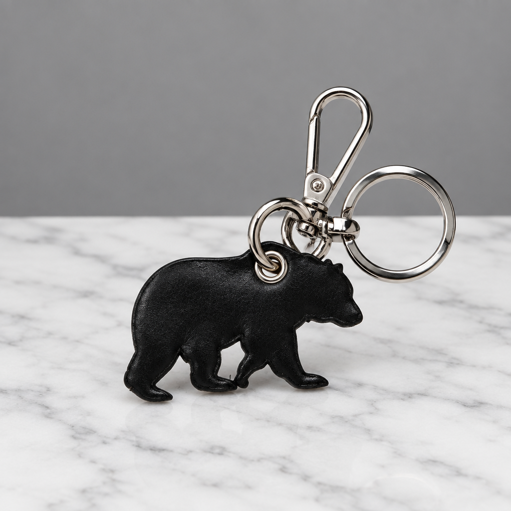 A black bear-shaped keychain with a silver metal clasp and key ring, photographed on a light off-white surface.